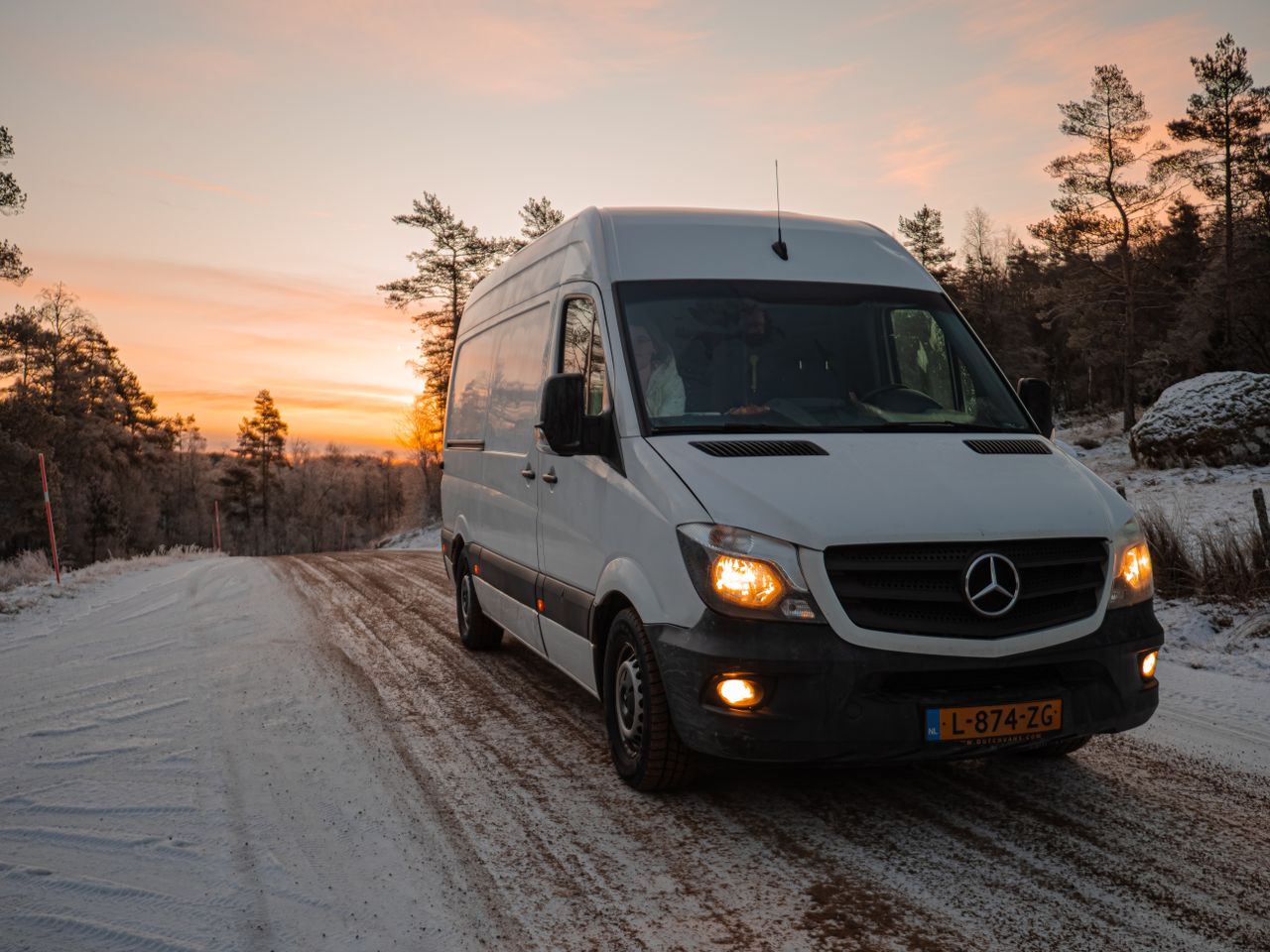 A van travels through the snowy landscapes of Norway at sunset, showcasing a serene winter road trip.